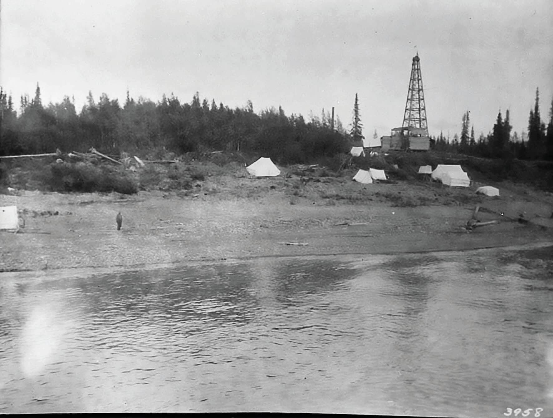 Black and white photos from the 1920s of an oil exploration site. Tents are set up around an oil rig close to a shore.
