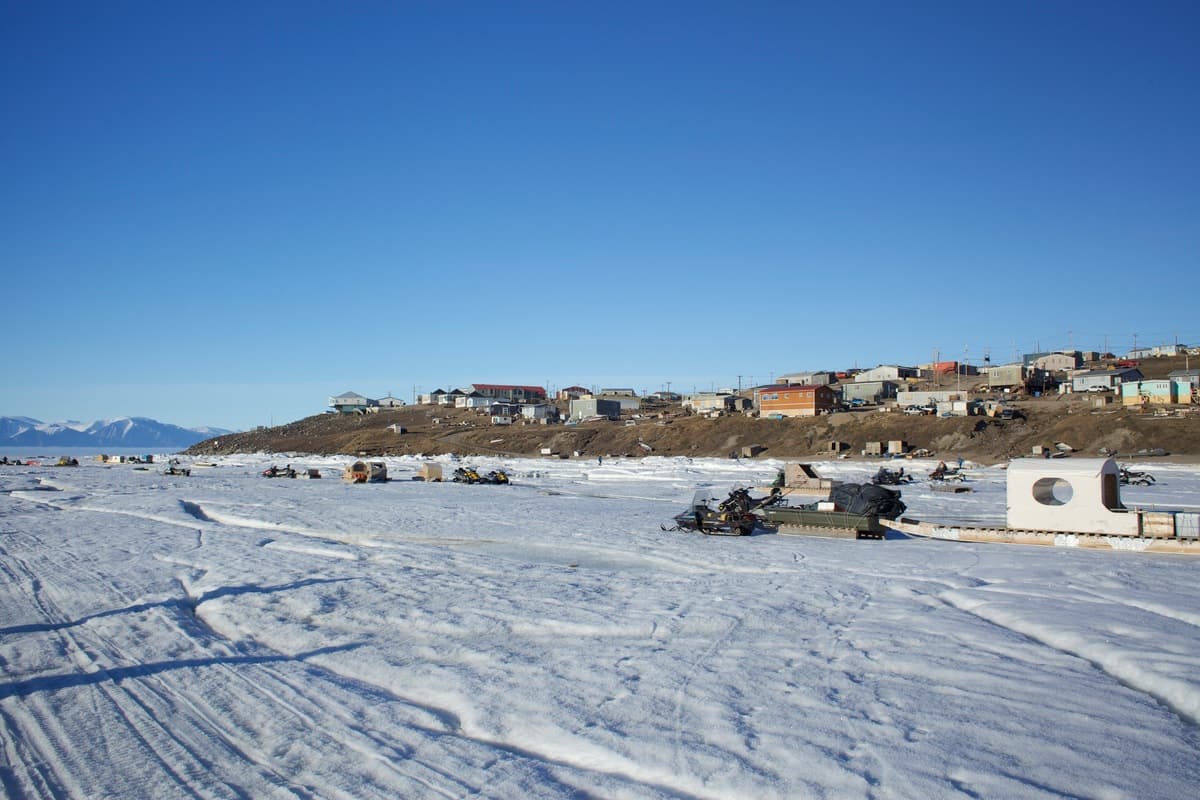 Houses on a hill in snowy Pond Inlet, Nunavut, Canada. It is a sunny. day and mountains are in the distance.