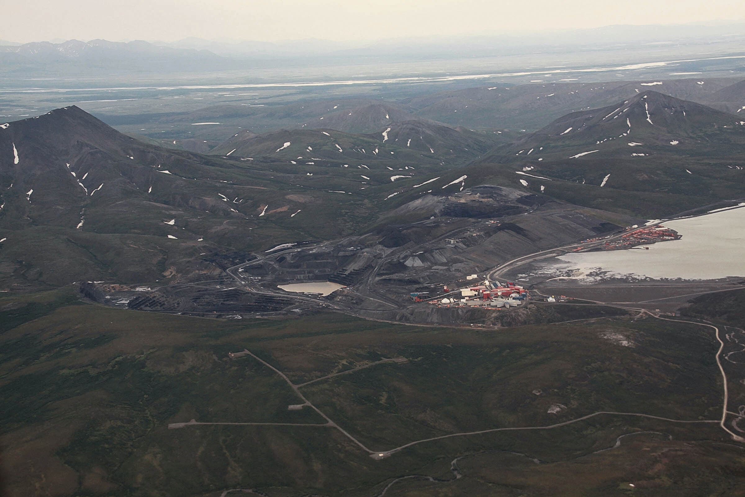 Industrial site in a mountainous Arctic region. There are snow capped mountains but otherwise the landscape is brown.