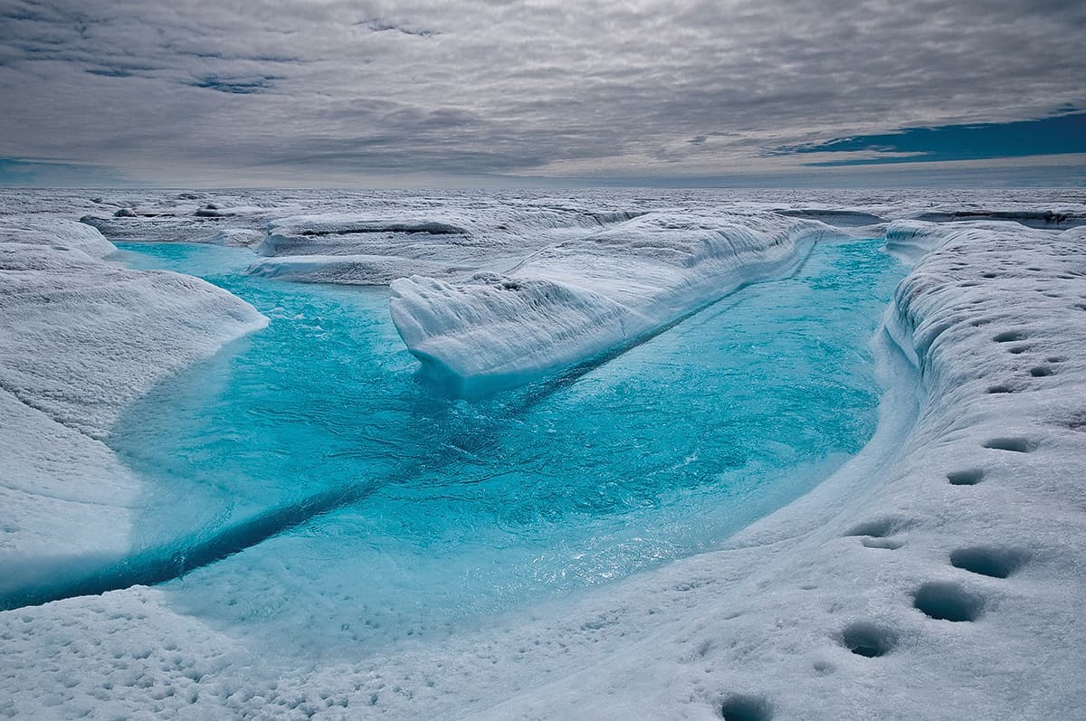 A large, meandering glacial-melt stream feeds a supraglacial lake in Greenland.