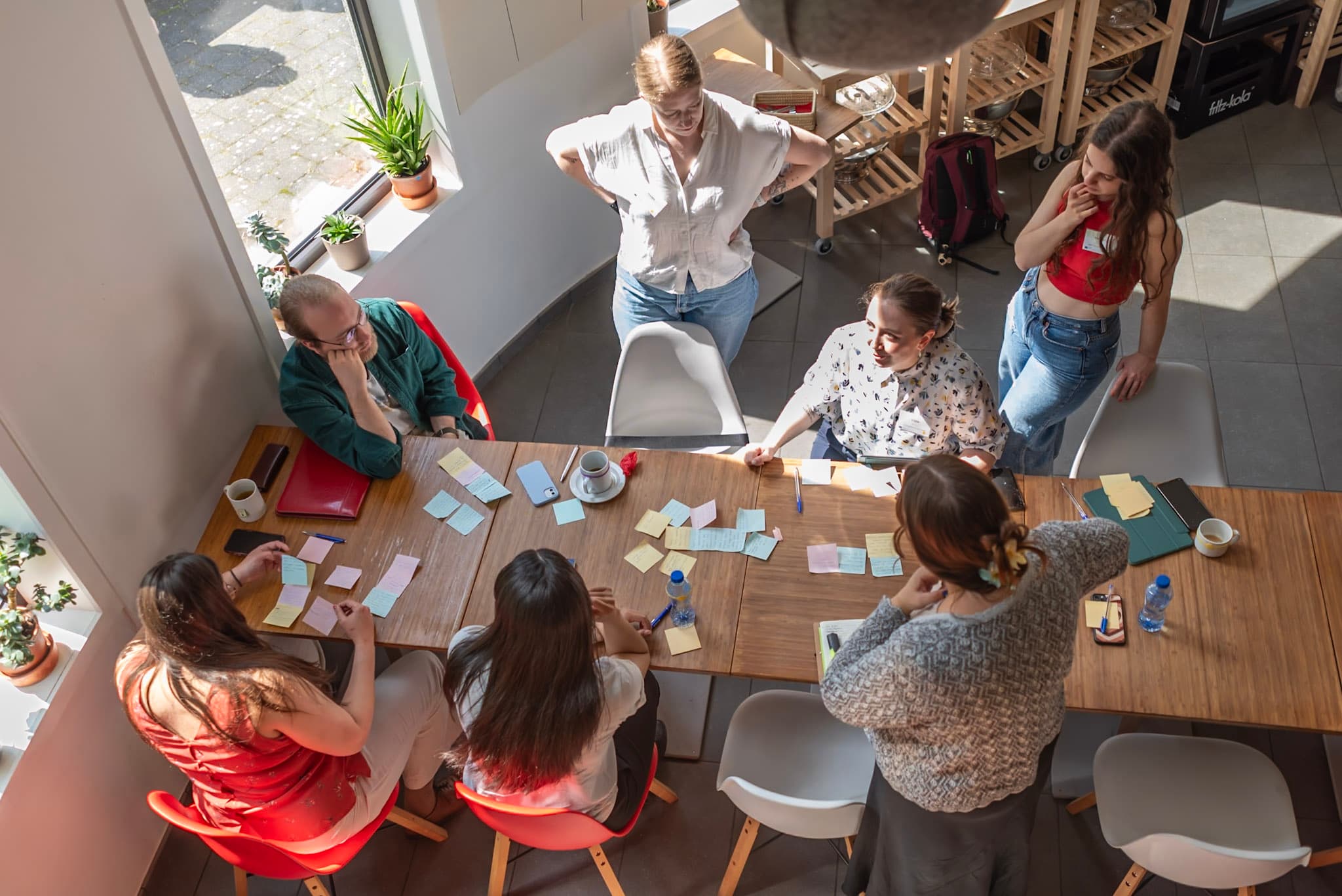 An image from above of seven youth at a workshop. There are post-it notes on a wooden table. The youth are involved in a discussion.