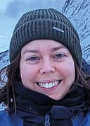 Ellen Bowler, in an Arctic landscape with snowy mountains in the background. Ellen's wearing a hat and winter clothes.