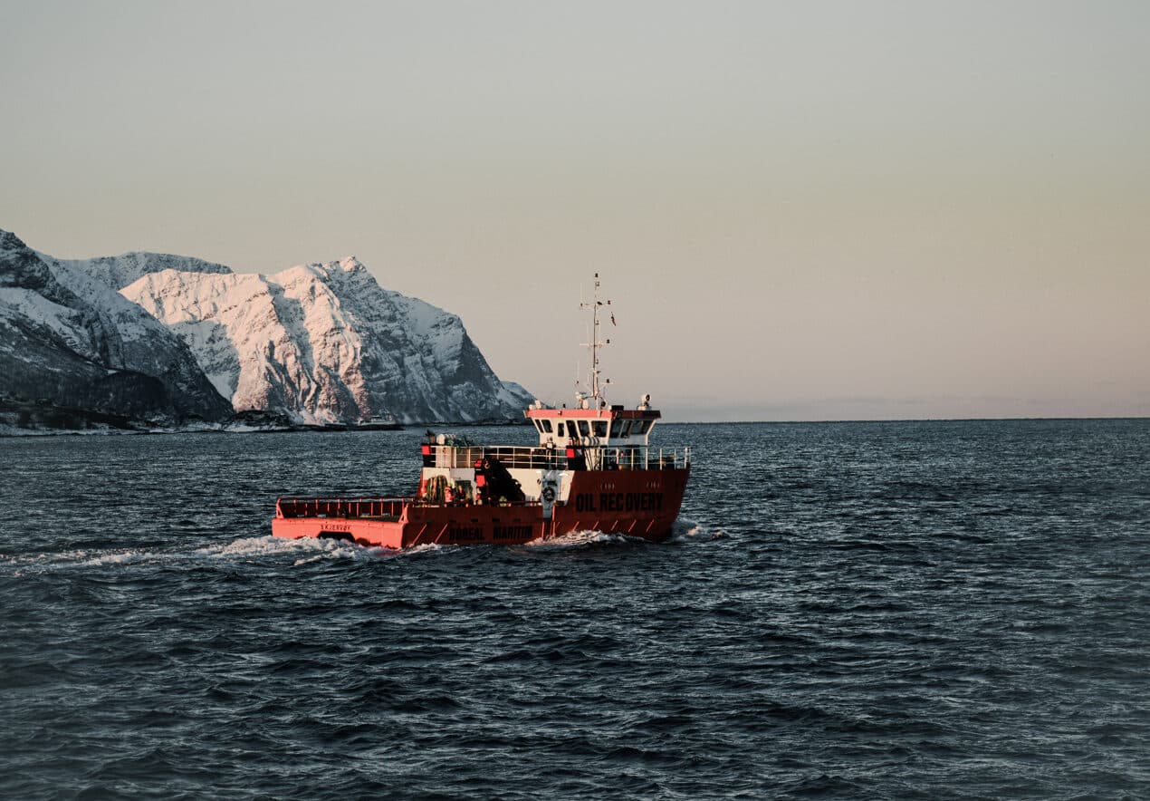 Orange underwater oil pumping vessel on the ocean. Snow-covered mountains visible in the background