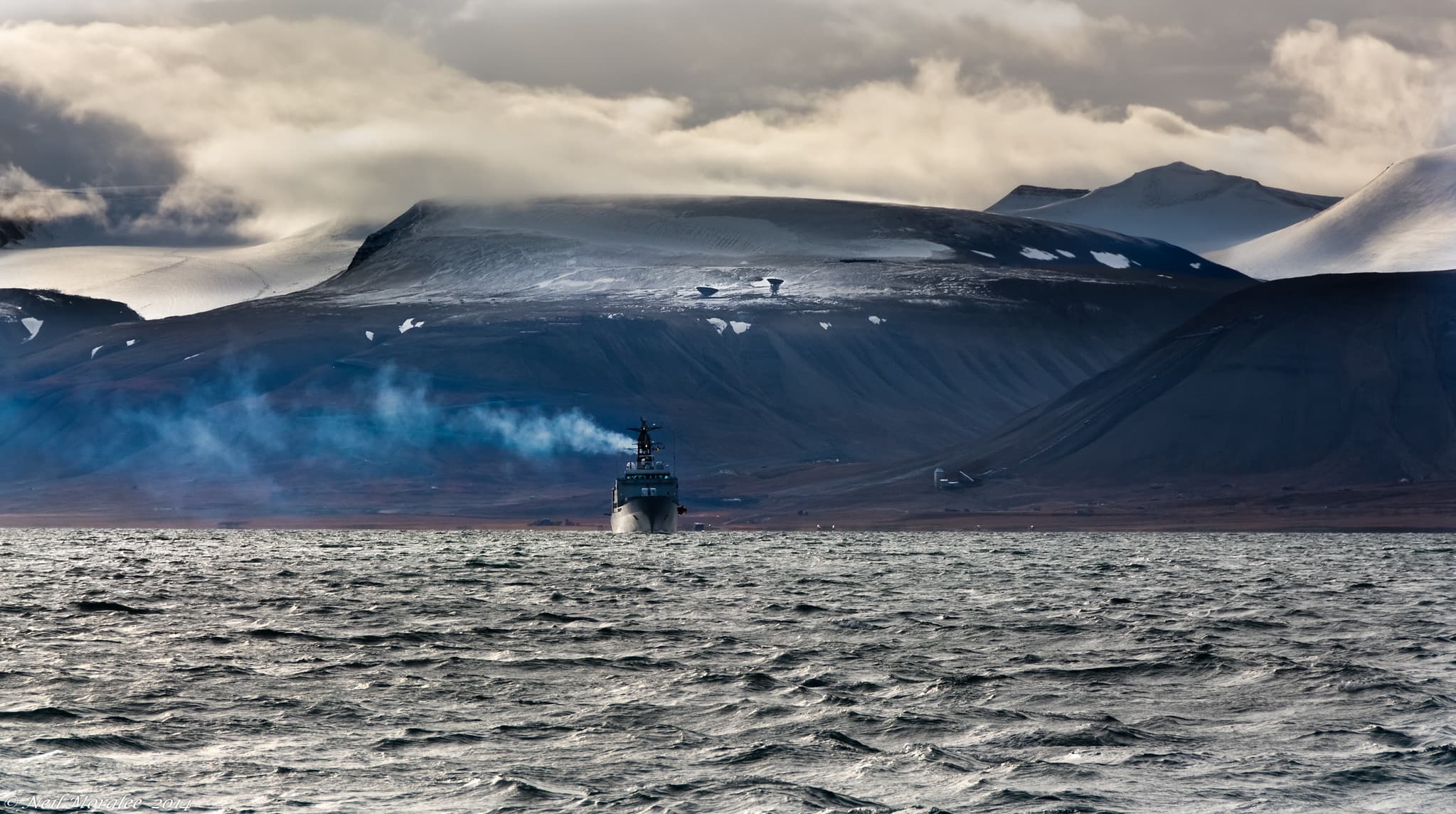 Ship near mountains and water with snowy mountains in the background.